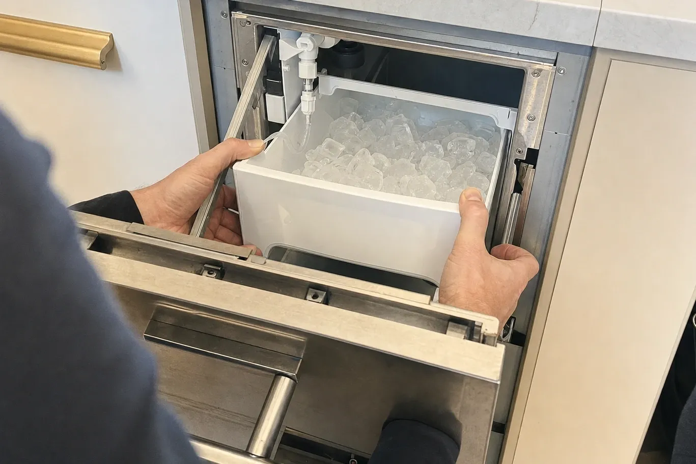 Hands sliding a bin full of clear cubes back into the ice maker drawer